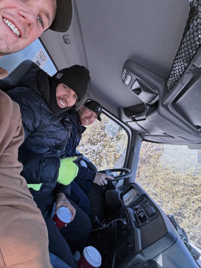 Three crew members in the cab of the truck with coffees on a cold morning