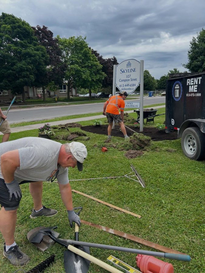 Crew laying fresh soil and plants in a garden bed at a commercial property sign